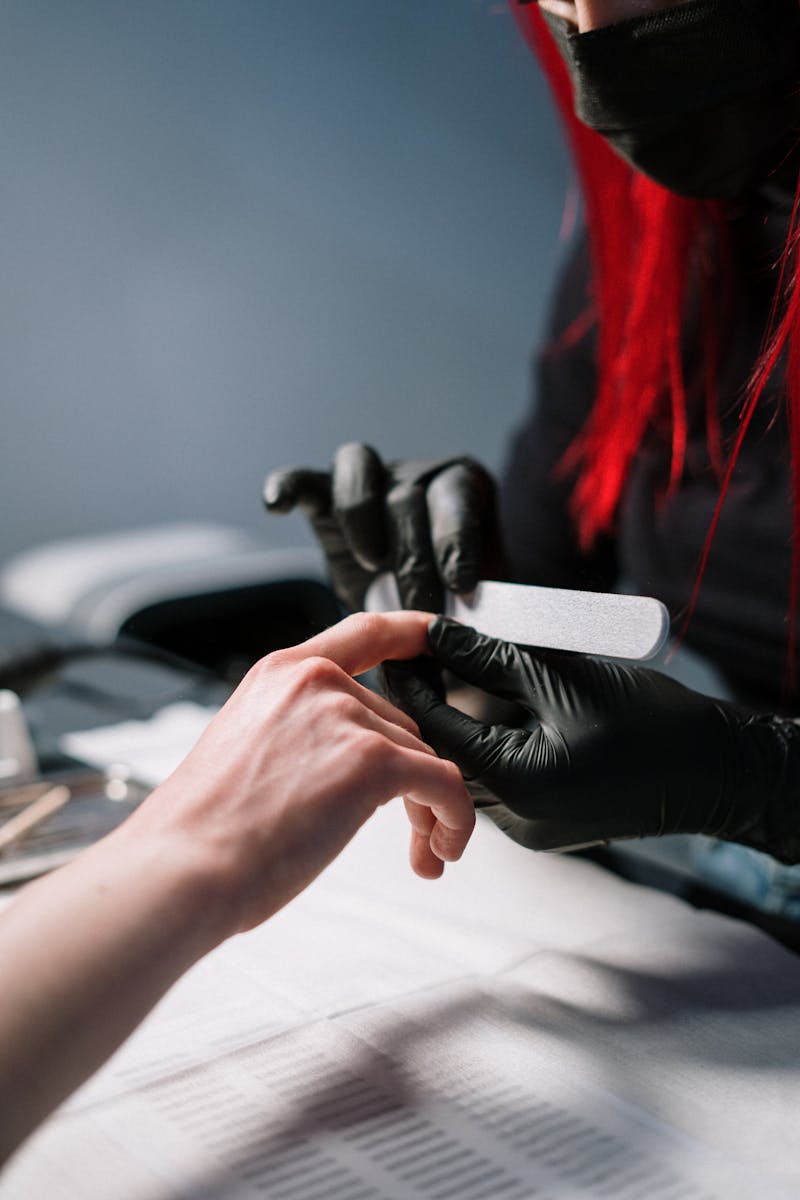 Close-up of a professional manicurist providing nail care with black gloves.
